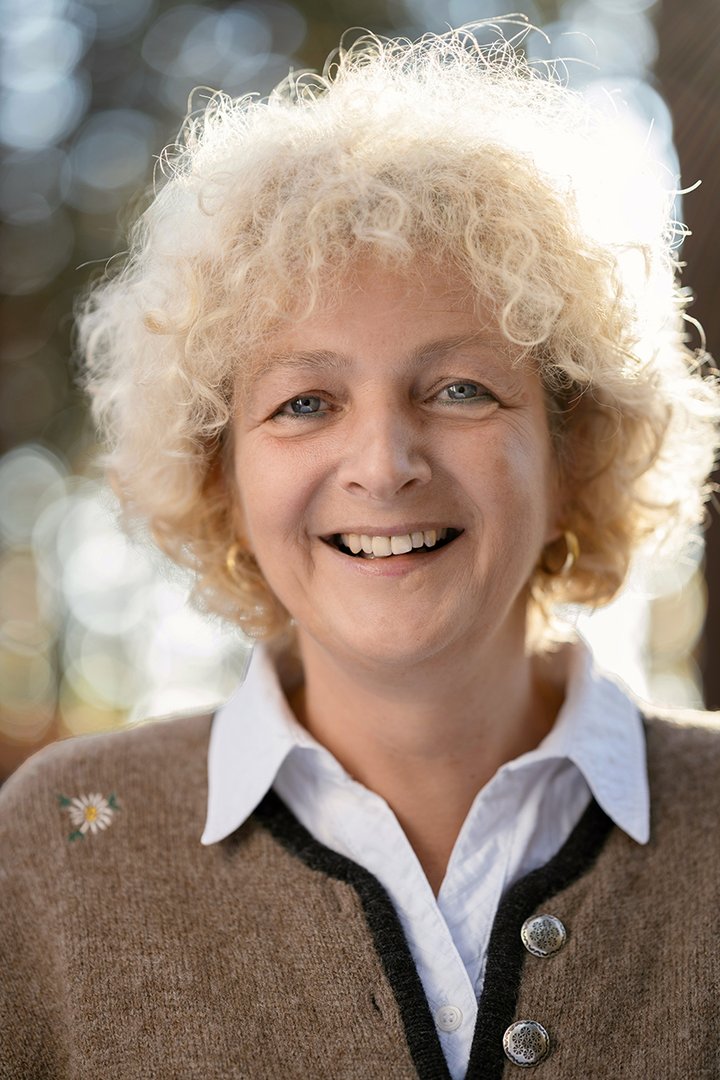 Foto: Tourismusverband Hausruckwald/Thomas Koller: Team_Brigitte Schiller Portraitfoto von Hausruckwald-Teammitglied Brigitte Schiller. Hellblonde, kurze Locken. Beiger Trachtenjanker mit weißer Hemdbluse. Sie lächelt und schaut direkt in die Kamera.