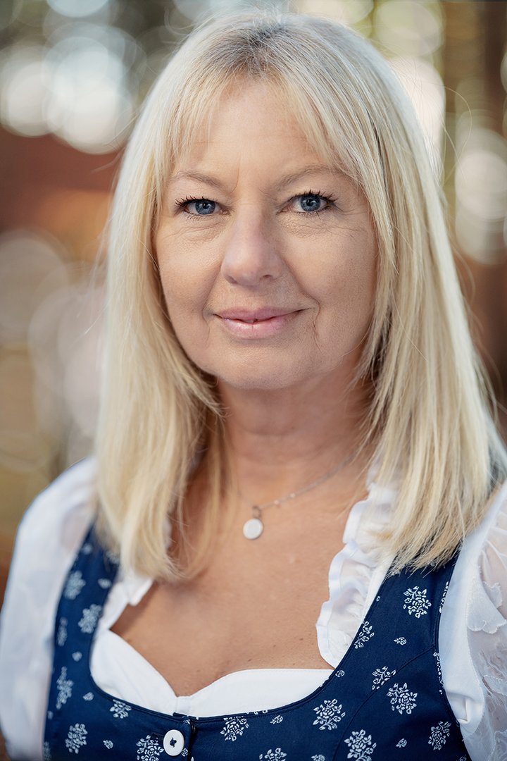Foto: Tourismusverband Hausruckwald/Thomas Koller: Team_Karin Klement Portraitfoto von Hausruckwald-Teammitglied Karin Klement. Blonde, schulterlange Haare, dunkelblaues Dirndl mit weißer Rüschenbluse. Sie lächelt und schaut direkt in die Kamera.